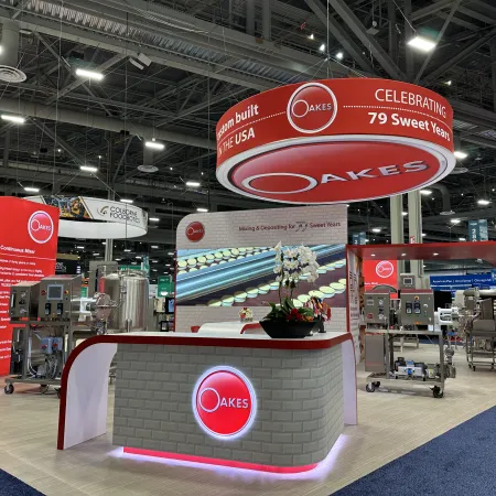 Oakes trade show booth with red and white branding celebrating 79 years, featuring industrial machines and display screens.
