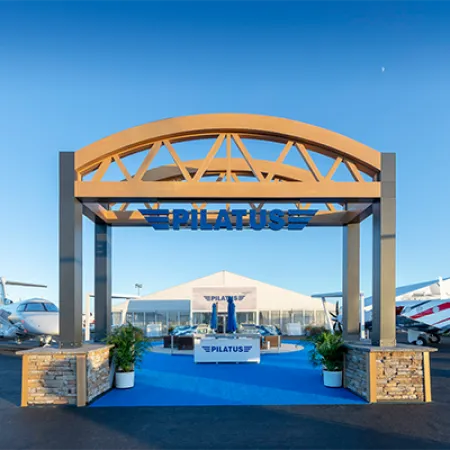 Pilatus aircraft exhibit with two private jets and branded booth under blue sky at airshow