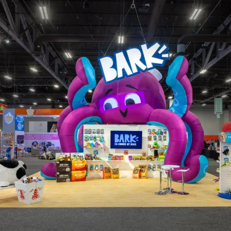 Colorful trade show booth with giant purple octopus, BARK logo, and dog products on display.