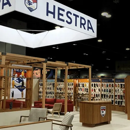 Hestra trade show booth with wooden displays showcasing various gloves and seating areas under large branded signs.