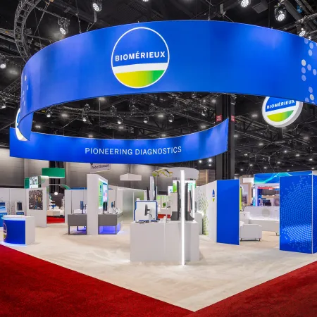 Biomerieux trade show booth with bright blue circular overhead banner and diagnostic displays on a red carpet floor.