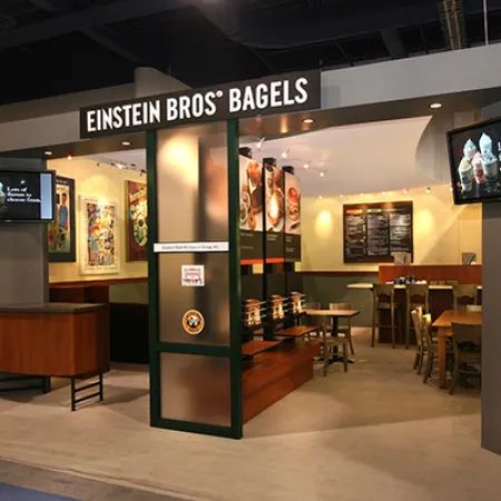 Einstein Bros Bagels cafe interior with seating, menu boards, and digital displays in a modern setup.