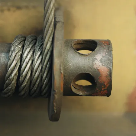 Close-up of steel cable wrapped around a rusted metal spool with industrial background.