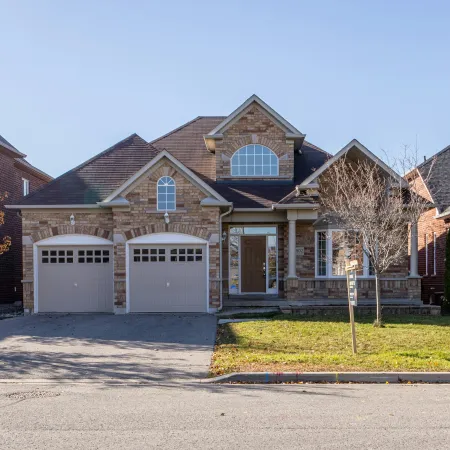 Two-story brick house with double garage, arched windows, and front lawn on a sunny day in a suburban neighborhood