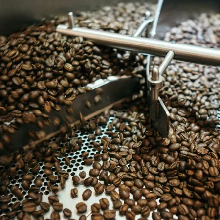 Close-up of roasted coffee beans being stirred inside an industrial cooling drum with metal stirring arms.