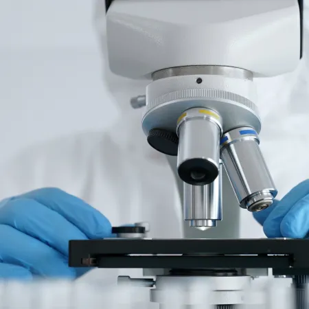 Scientist wearing blue gloves using a microscope for close-up scientific research in a lab environment.