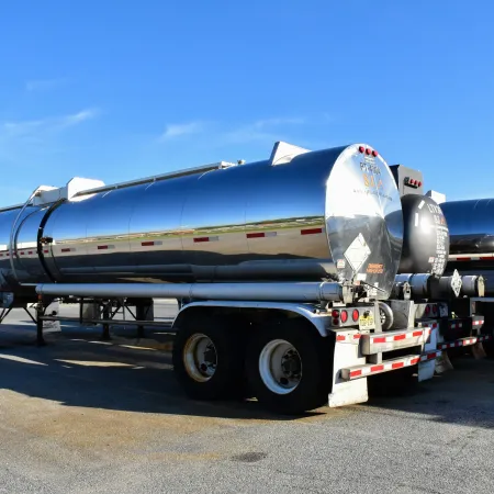Shiny silver tanker trucks parked in a row under clear blue sky in an industrial lot.