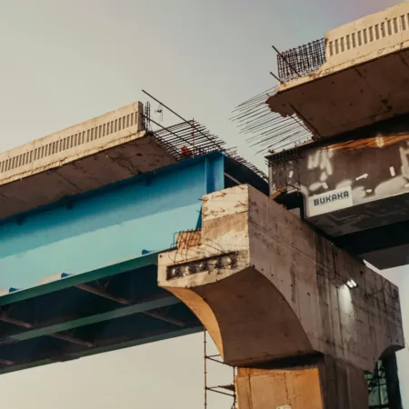 Close-up view of a partially constructed concrete and steel bridge with exposed rebar and beams at dusk.