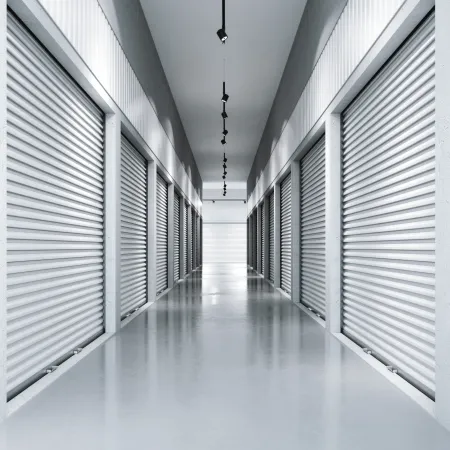 Long corridor with closed silver metal storage unit doors on both sides and overhead lights in a clean facility.