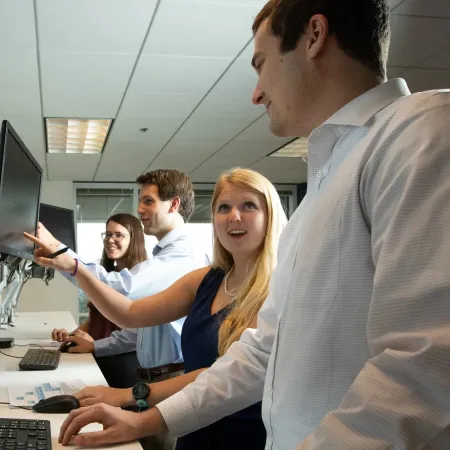Team of four professionals collaborating at standing desks with multiple monitors in a bright office space