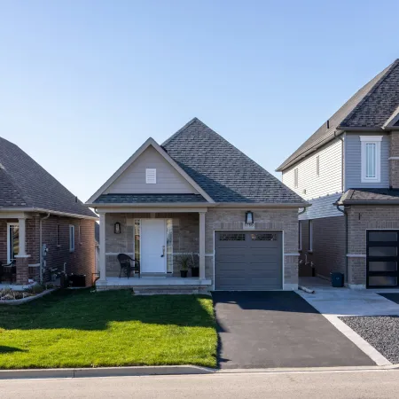 Suburban residential street with three modern single-family houses and well-maintained lawns under clear blue sky