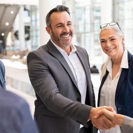 Business professionals smiling and shaking hands in a modern office setting during a meeting.