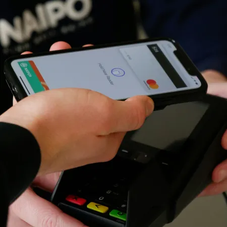 Person holding smartphone with digital wallet app over a card payment terminal for contactless payment.