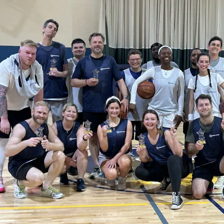 Mixed group of basketball players posing in gym holding trophies and basketballs after a game celebration.