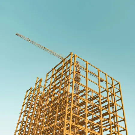 Roof worker in safety harness fixing shingles with a tool on a sunny day on a residential house roof.