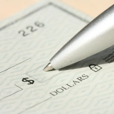 Close-up of a pen poised to fill out the dollar amount on a blank check.