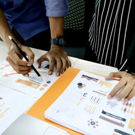 Two people analyzing charts and graphs on printed reports with business data and infographics on a table.