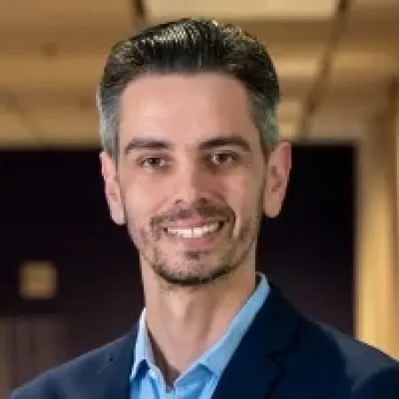 Smiling man with short dark hair wearing a blue suit jacket and light blue shirt in office setting