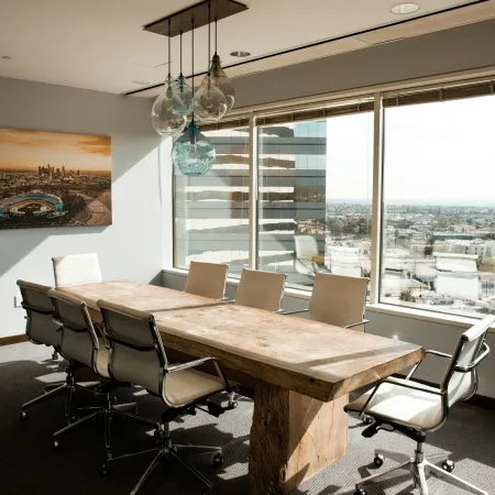 Bright modern conference room with wooden table, white chairs, city view, and hanging glass pendant lights.