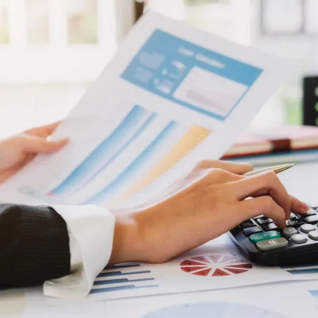 Person analyzing charts and graphs while using a calculator to review financial data and reports.