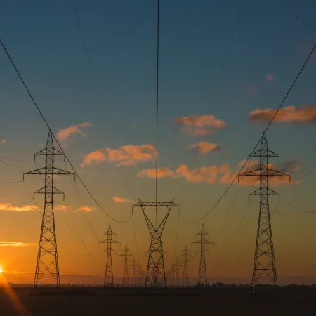 Electric power transmission towers at sunset with clear sky and clouds over flat landscape.