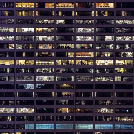 Night view of office building with illuminated windows showing various office spaces and desks.