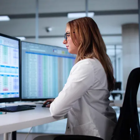 Professional woman analyzing data on dual monitors in modern office environment with spreadsheets and charts