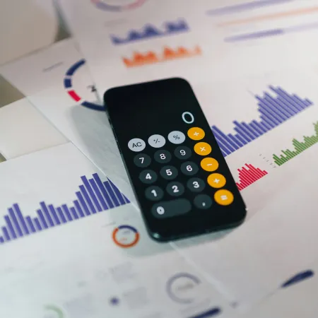 Smartphone calculator app on financial charts with colorful graphs and data analysis sheets on a desk.
