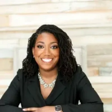 Smiling professional woman with braided hair in black blazer sitting with arms crossed indoors