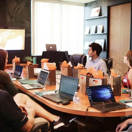 Business team attending a presentation in a modern conference room with laptops and gift bags on the table