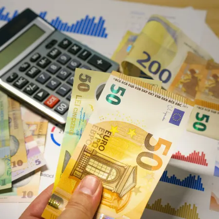 Hand holding 50 euro banknotes with calculator and financial charts on table