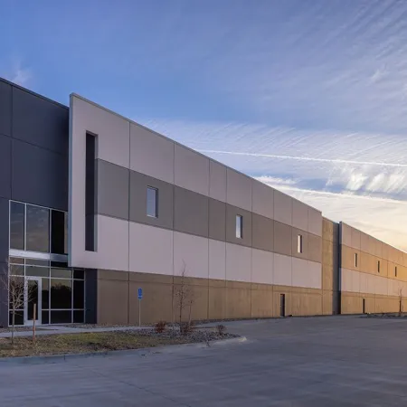 Modern industrial warehouse building with gray and beige panels under a blue sky at sunset.