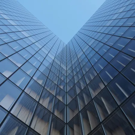 Glass skyscraper buildings converging with reflections under a clear blue sky, viewed from below.