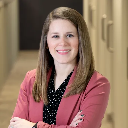 Confident woman in a pink blazer and black polka dot shirt standing with arms crossed indoors