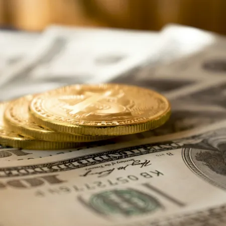 Stack of gold Bitcoin coins placed on US 100 dollar bills representing cryptocurrency and fiat currency exchange.