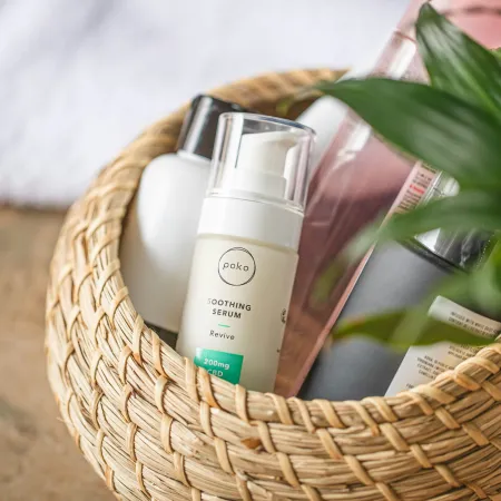 Woven basket holding skincare bottles including Poko Soothing Serum and a green plant partially visible