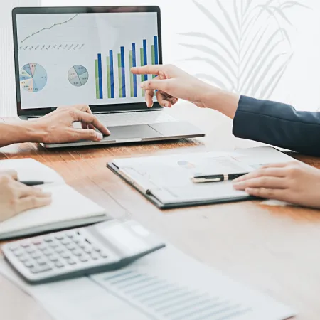 Two professionals analyzing financial graphs and charts on a laptop during a business meeting.