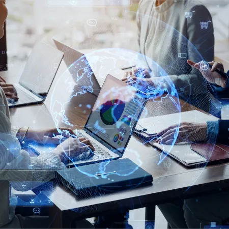 Business team collaborating with laptops, digital charts, and a holographic globe overlay in an office.