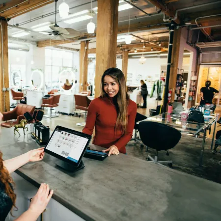 Customer paying at a modern hair salon reception with a smiling receptionist and digital payment system.