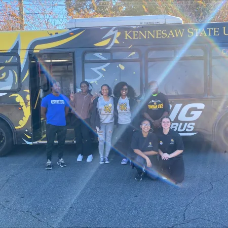 a group of people posing in front of a yellow bus