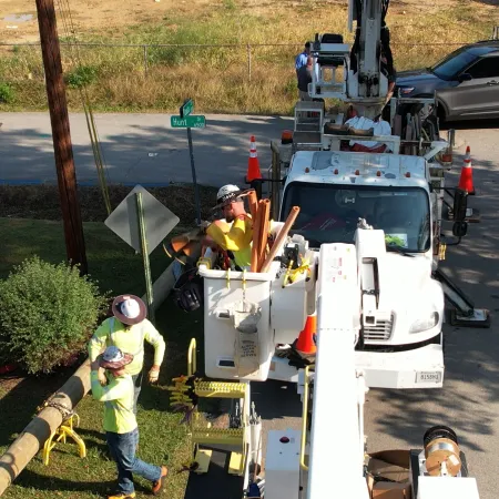 Utility workers repair power lines using bucket trucks on a residential street with safety cones around.