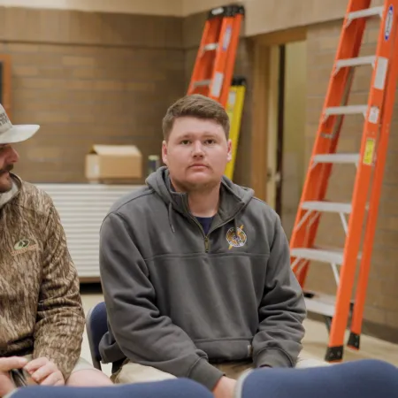 Two young men in casual hoodies sitting on chairs in a room with ladders and a brick wall background