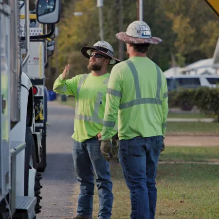 Two utility workers in high-visibility clothing standing by a work truck near a road sign that says END.