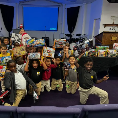 Group of children excitedly holding new toy sets inside a room with musical instruments and projector screen.