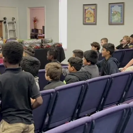 Children seated in rows of chairs attending an indoor event or presentation in a community room.