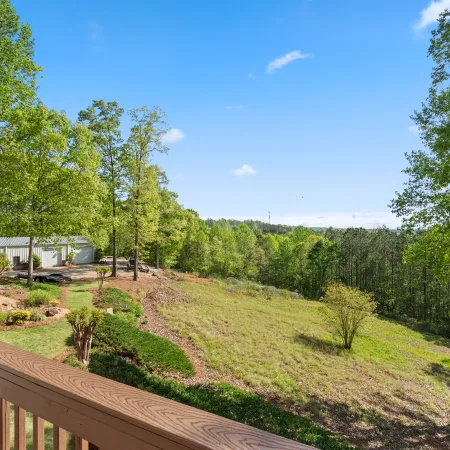 Scenic backyard view from wooden deck overlooking grassy hill, trees, and blue sky on a sunny day