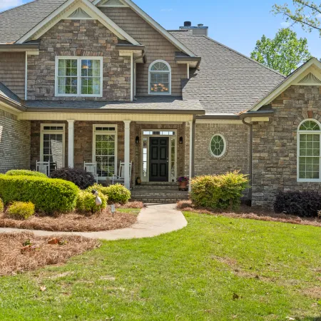 Stone and brick suburban house with landscaped front yard, shrubs, and a black front door on a sunny day.