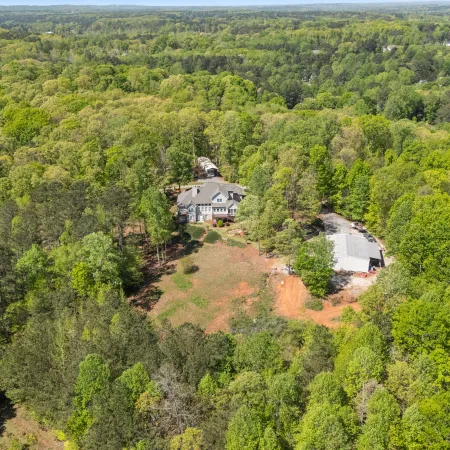 Aerial view of a large home and outbuilding surrounded by dense green forest in a rural area