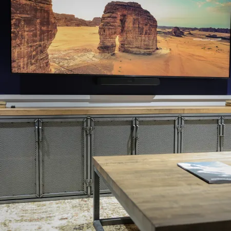 Modern living room with a large flat screen TV showing desert rock formations over a metal cabinet and wooden table.