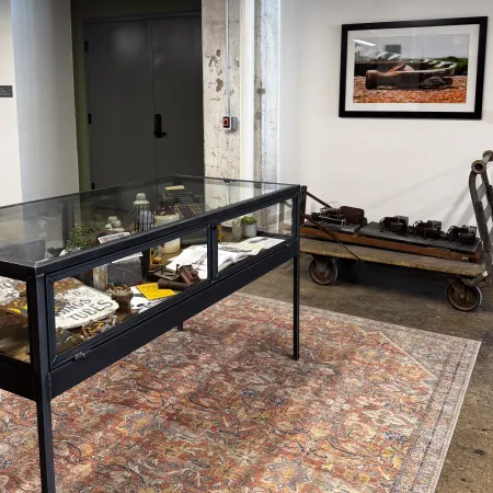 Industrial-themed museum display with artifacts in glass case and vintage tools on cart against white walls.